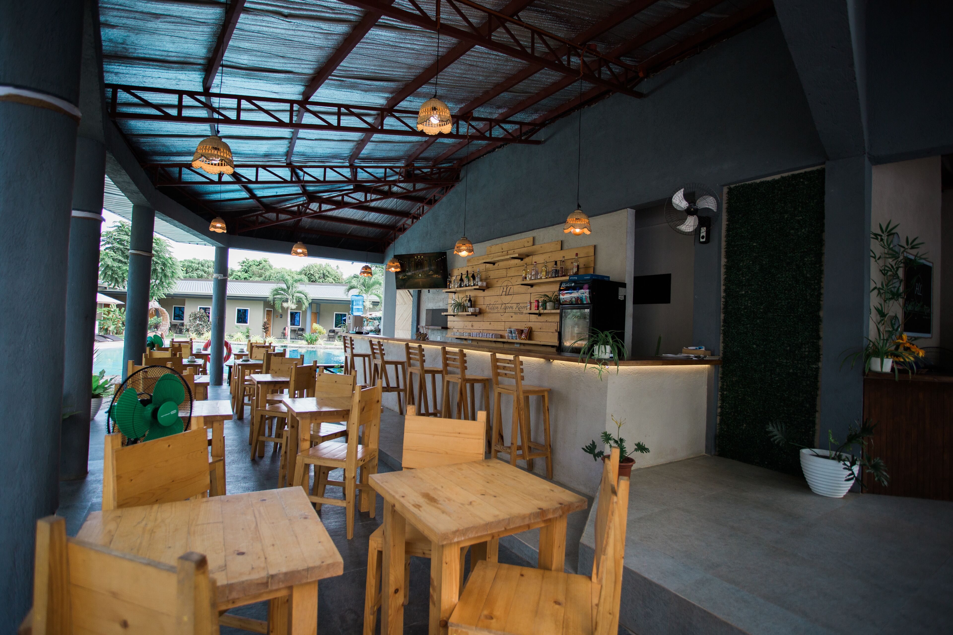 An indoor dining area with wooden tables and chairs, a bar counter, and a view of the outside.