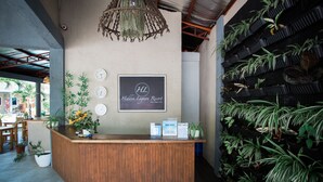 A reception desk with a wooden counter, a sign for Hidden Lagoon Resort, and a wall of potted plants. - Hidden Lagoon Resort (Panglao)