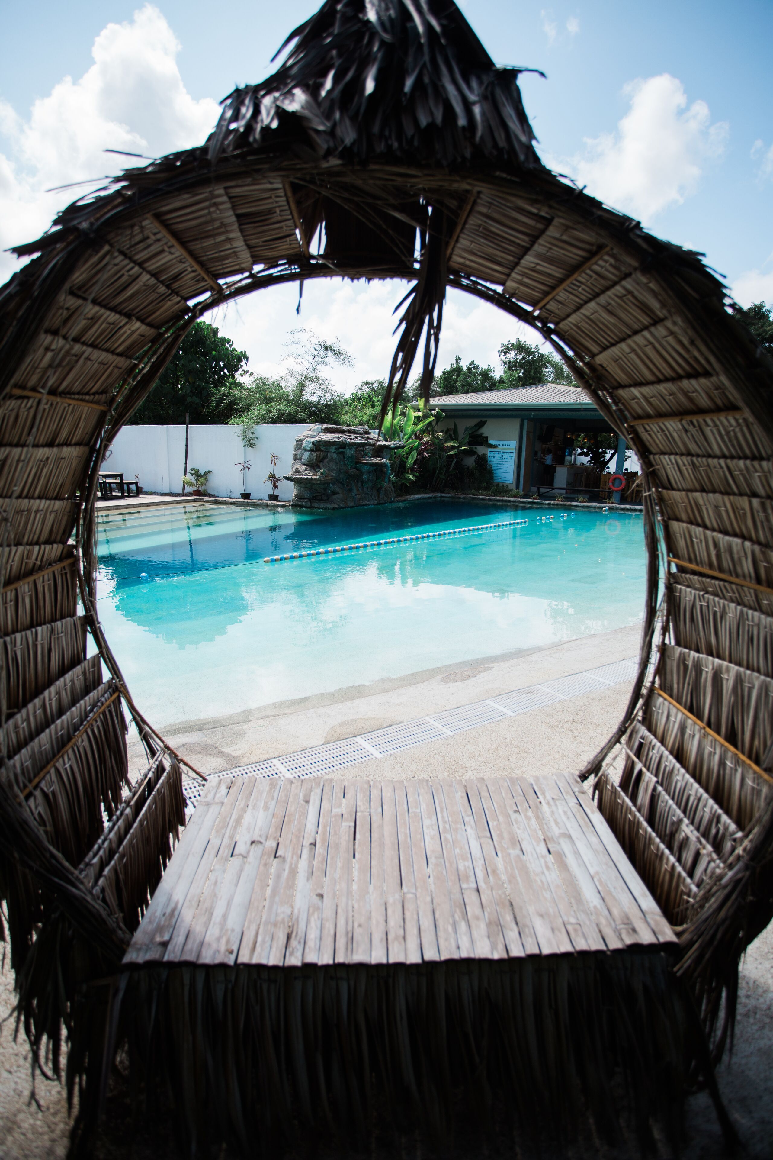 A circular wooden structure framing a swimming pool with a rocky backdrop and a building in the distance.