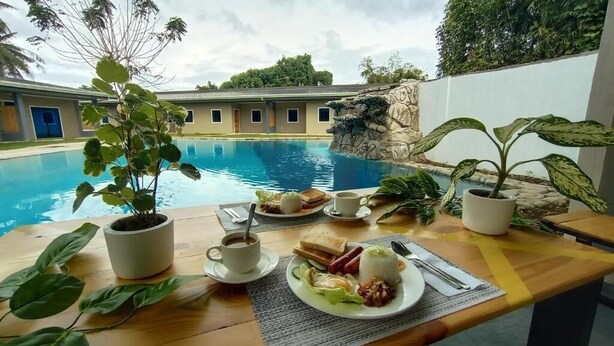 A dining table with breakfast items, a coffee cup, and potted plants by a poolside. - Hidden Lagoon Resort (Panglao)