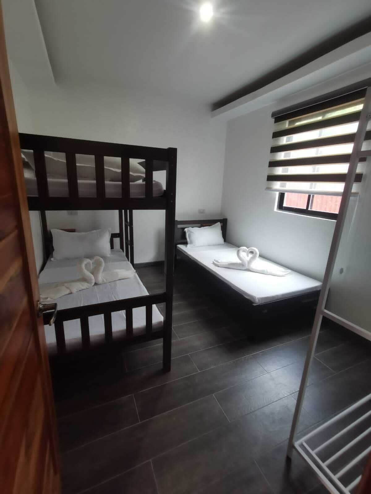Habitación compacta con dos literas y una cama individual, que cuenta con una ventana con persianas y un balcón visible.