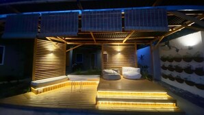 A covered outdoor area with a wooden deck, two white cushioned seating areas, and solar panels on the roof. - Hidden Lagoon Resort (Panglao)