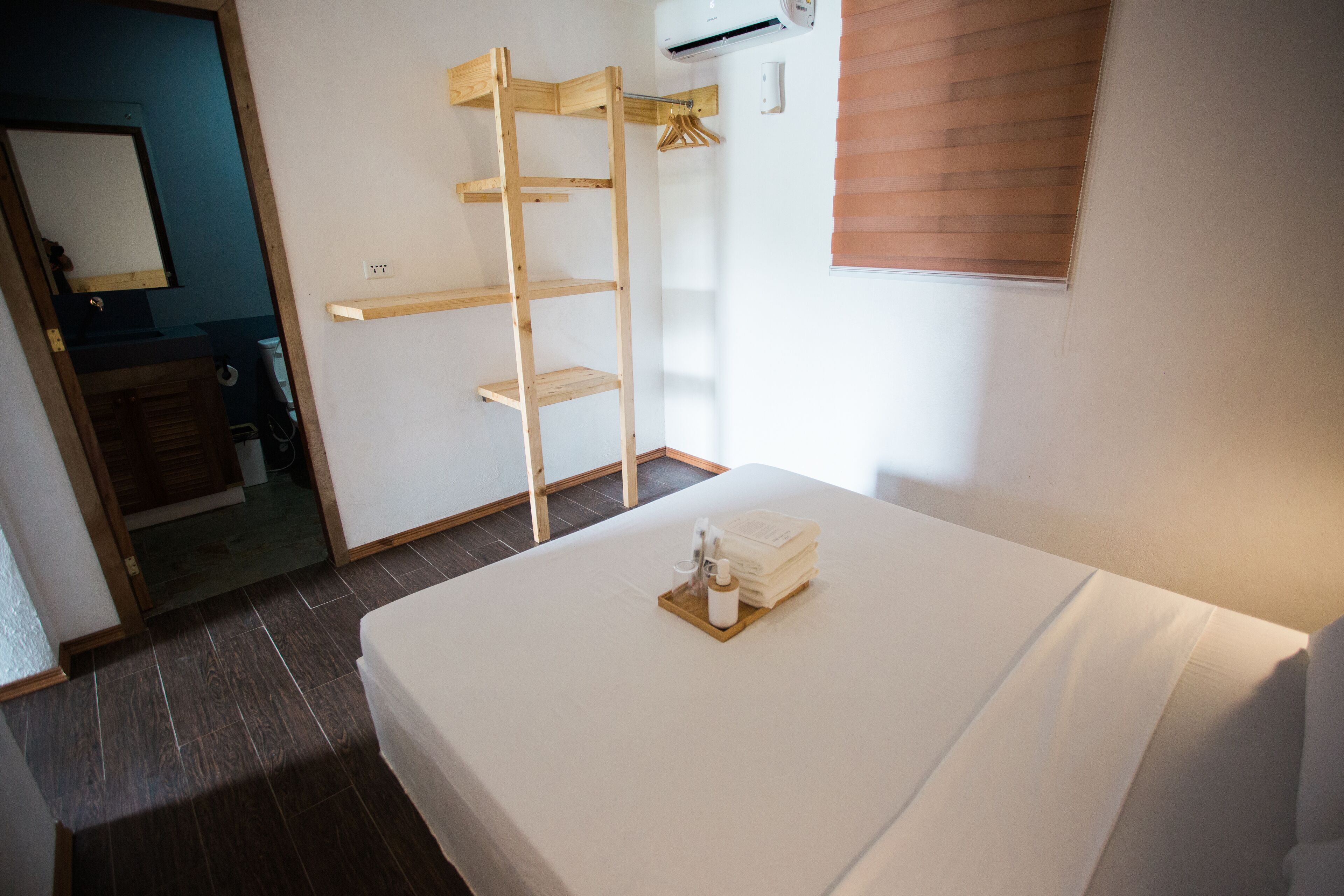 Habitación de hotel con cama, estantería de madera, espejo y ventana con persianas.
