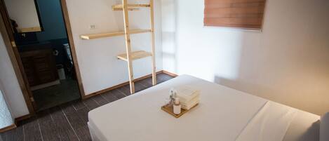 Habitación de hotel con cama, estantería de madera, espejo y ventana con persianas.