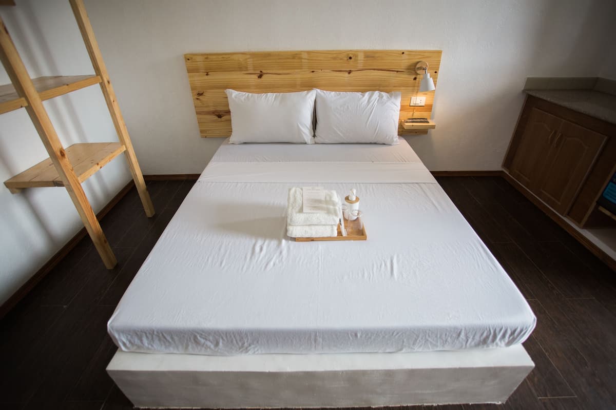A neatly made bed with white linens, a wooden headboard, and a bedside table with a lamp.