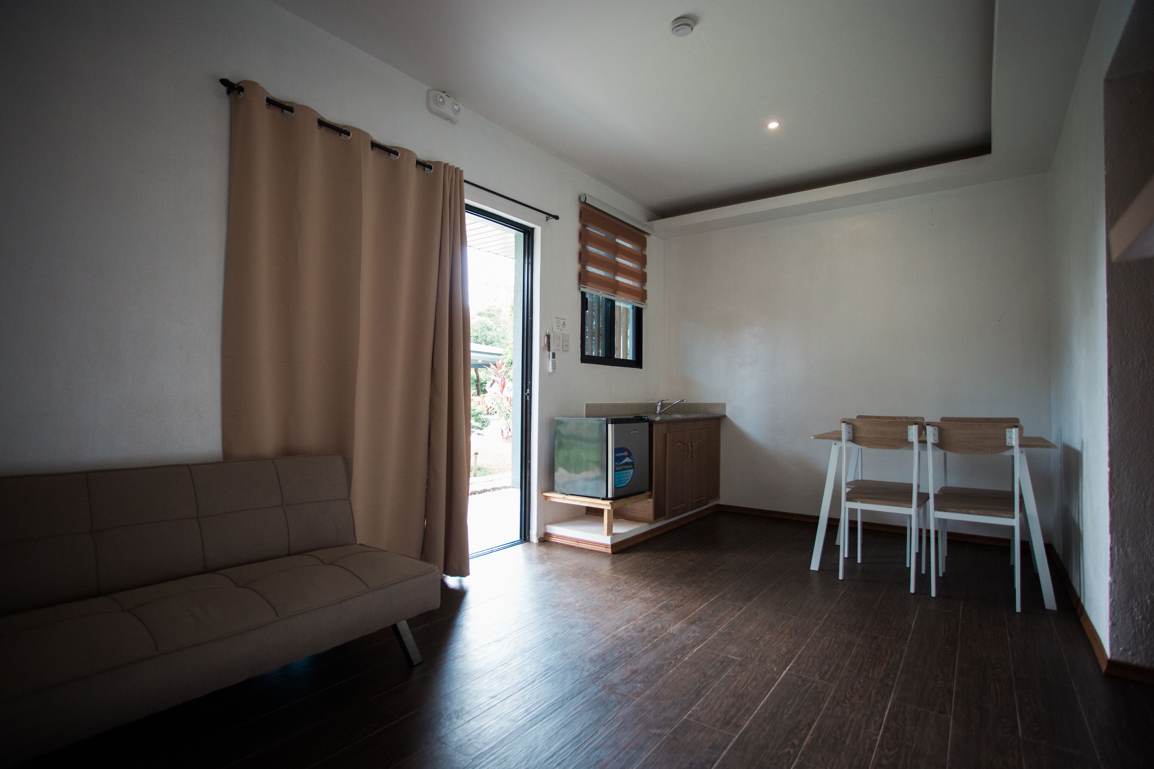 A living room with a sofa, a TV on a wooden stand, and a dining area with chairs.