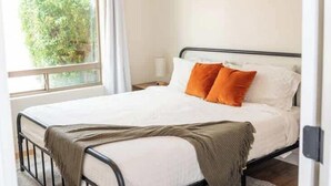 Une chambre à coucher avec un lit, un ventilateur de plafond, une fenêtre avec des rideaux et une vue sur la verdure à l’extérieur.