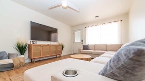 Un salon moderne avec un canapé, une table basse, un téléviseur fixé au mur et un ventilateur de plafond.