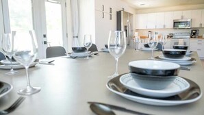 Une table à manger dressée avec des assiettes, des bols et des verres à vin, avec une cuisine en arrière-plan.