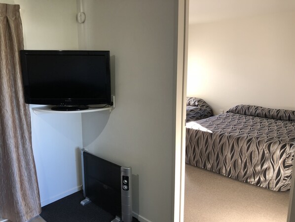 Habitación de hotel con televisión de pantalla plana montada en la pared, cama con ropa de cama estampada y piso alfombrado.
