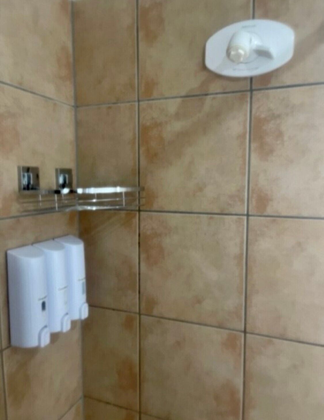 A bathroom with beige tiles, a hand dryer, and a soap dispenser.