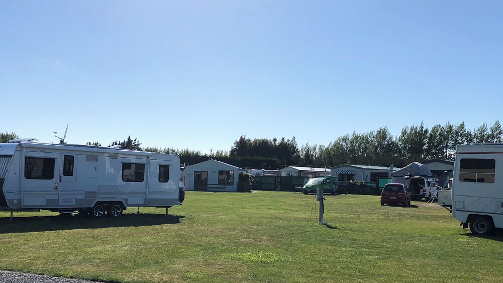 Un terrain de camping où plusieurs camping-cars et remorques sont stationnés sur un champ d’herbe.