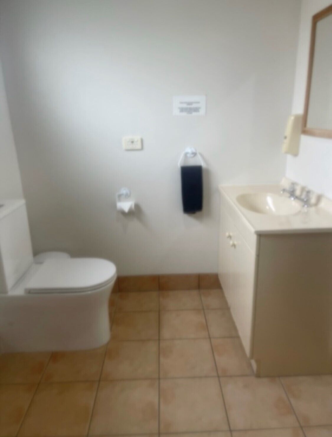 Een kleine badkamer met toilet, wastafel en een zeepdispenser.