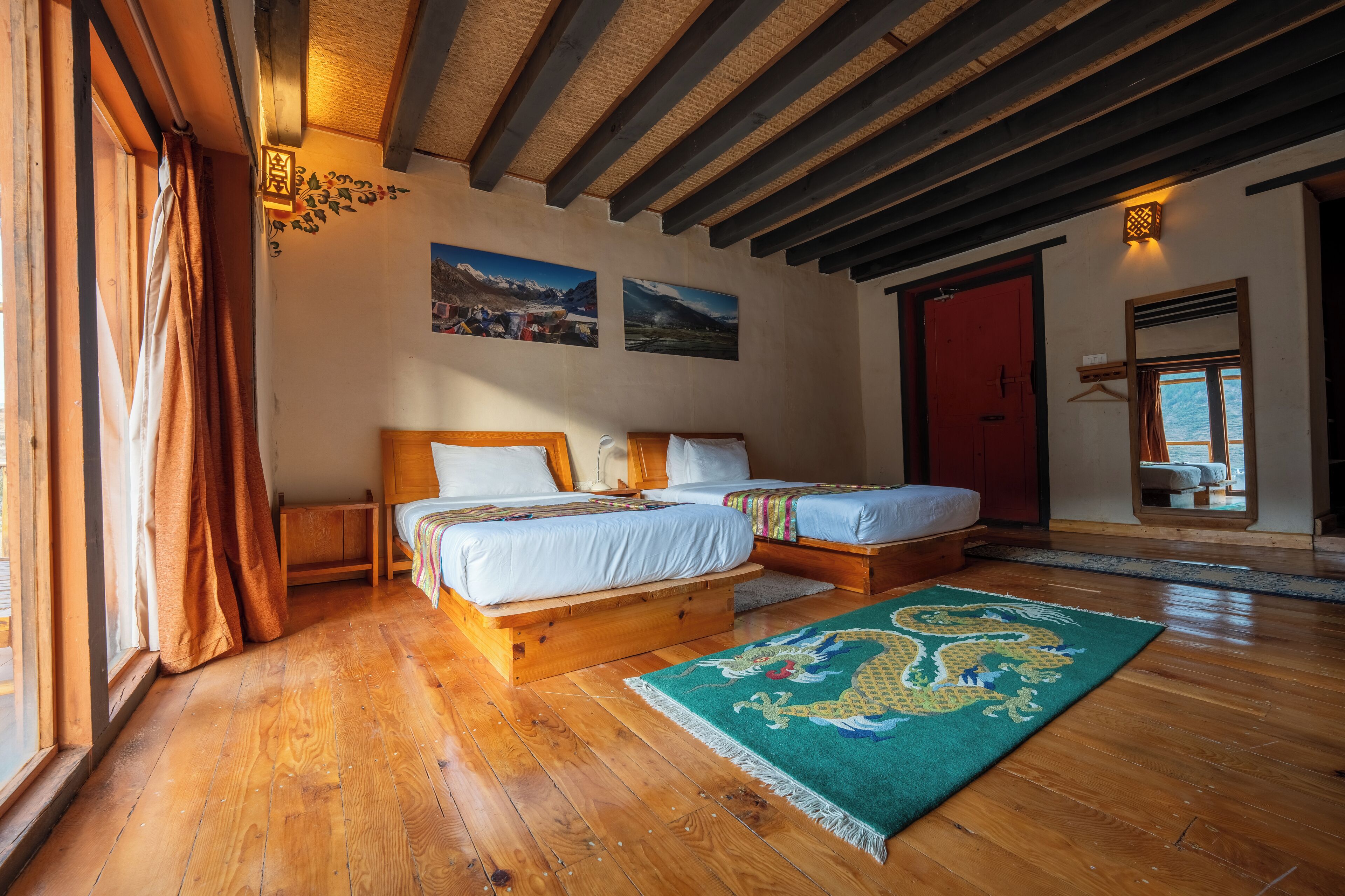 Una stanza con due letti di legno, un pavimento in legno, un tappeto verde con motivo decorativo e una porta rossa.