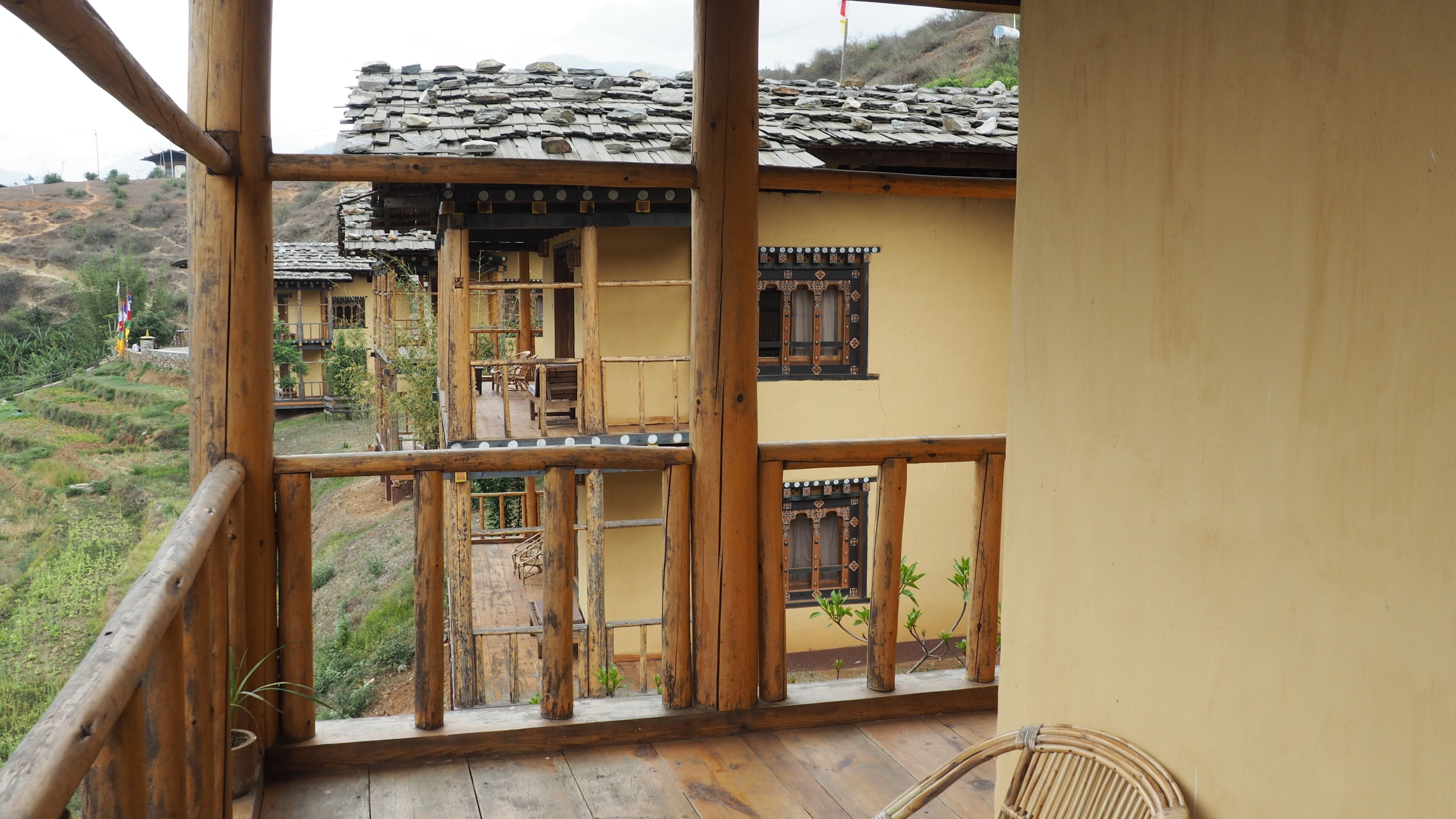 Una casa de madera tradicional con balcón, campos en terrazas al fondo y una vista despejada del paisaje circundante.
