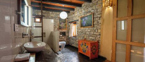 A rustic bathroom with a stone wall, wooden beams, a large sink, and a wooden cabinet.