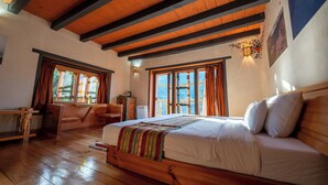 Un dormitorio con suelo de madera, una cama grande, un escritorio y una ventana con cortinas.