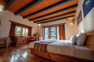 Un dormitorio con suelo de madera, una cama grande, un escritorio y una ventana con cortinas.