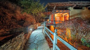 Un sendero de piedra conduce a un edificio tradicional con una cerca de madera y un interior iluminado.