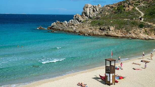 A beach with clear turquoise water, rocky cliffs, and a lifeguard tower.