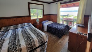 Een kamer met twee bedden, een raam met jaloezieën, een lamp en uitzicht op een meer.