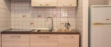 A kitchen with light wood cabinets, a stainless steel sink, and a white refrigerator.