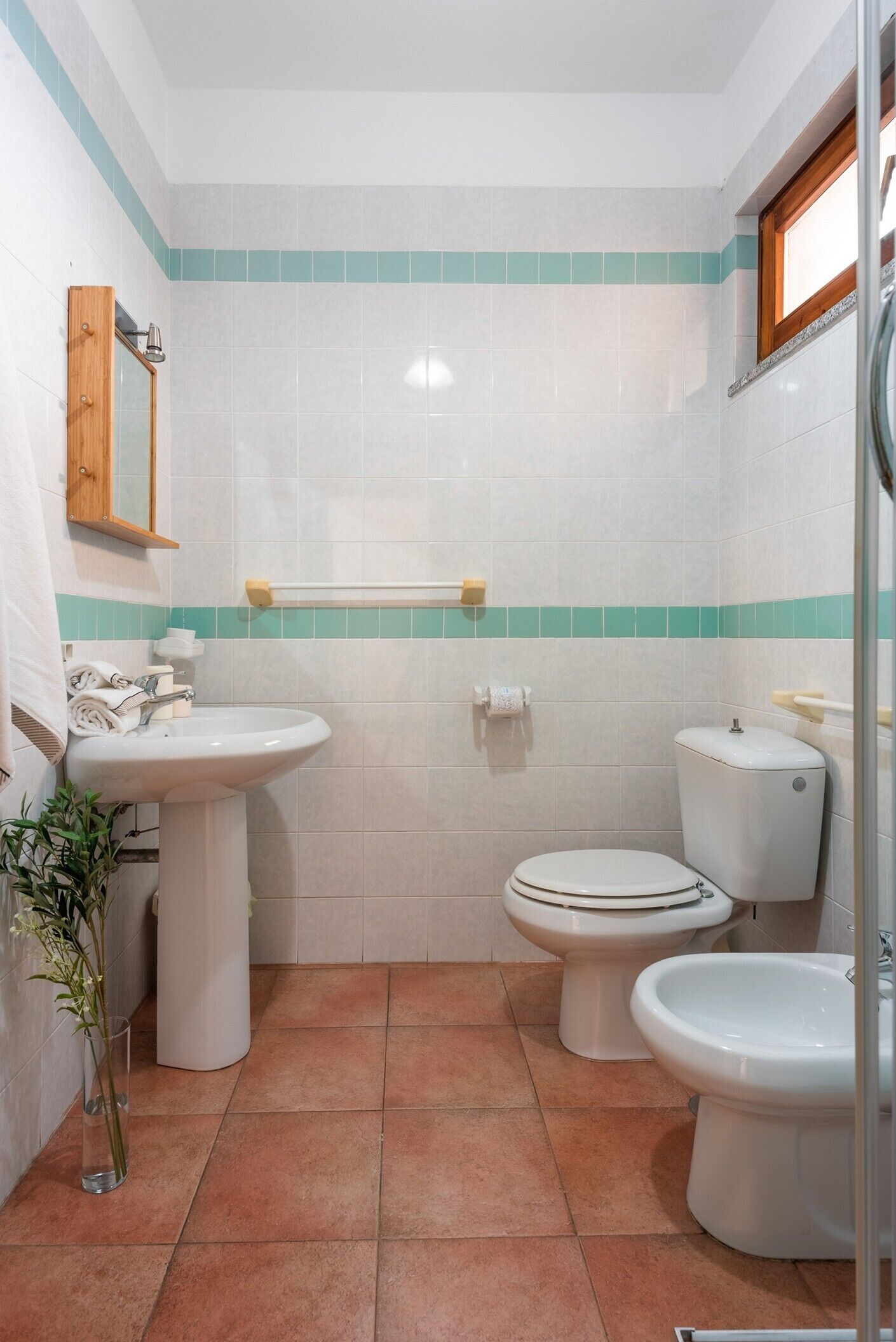 A compact bathroom with a sink, two toilets, and a mirror.