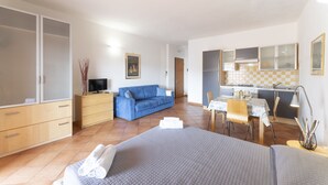 A bedroom with a bed, a blue sofa, a desk with a chair, and a kitchenette.