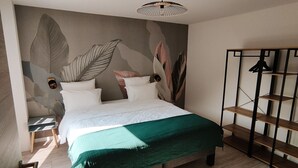 Un dormitorio con cama, colcha verde, pared con motivos de hojas y suelo de madera.