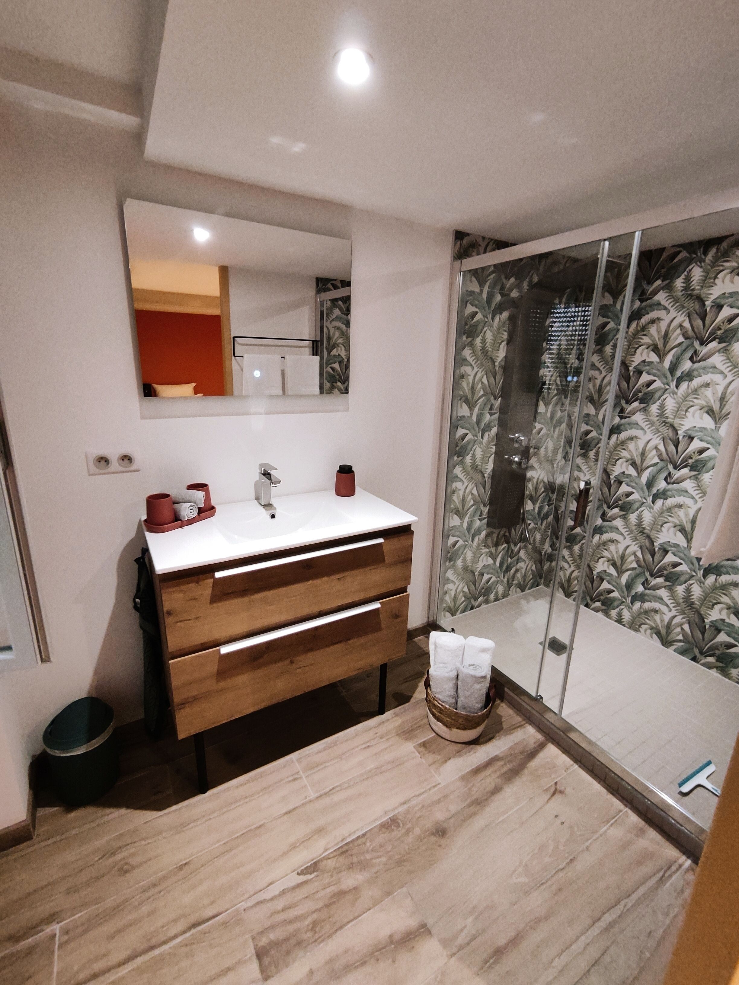 A bathroom with a wooden vanity, a white sink, and a glass shower enclosure with a leaf-patterned shower curtain.