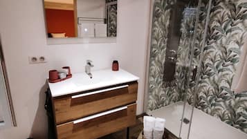 A bathroom with a wooden vanity, a white sink, and a glass shower enclosure with a leaf-patterned shower curtain.