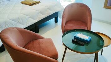 Een slaapkamer met een bed, twee fauteuils, een glazen tafel en uitzicht op groen.