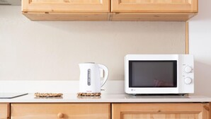 Una cocina con armarios de madera, una encimera blanca, un hervidor eléctrico blanco y un microondas blanco.