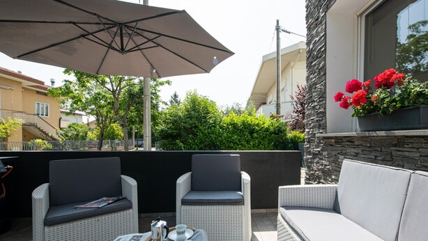 An outdoor seating area with wicker furniture, a table with a tray of croissants, and a large umbrella. - La Casa di Guido in Gabicce Mare (Gabicce Mare)