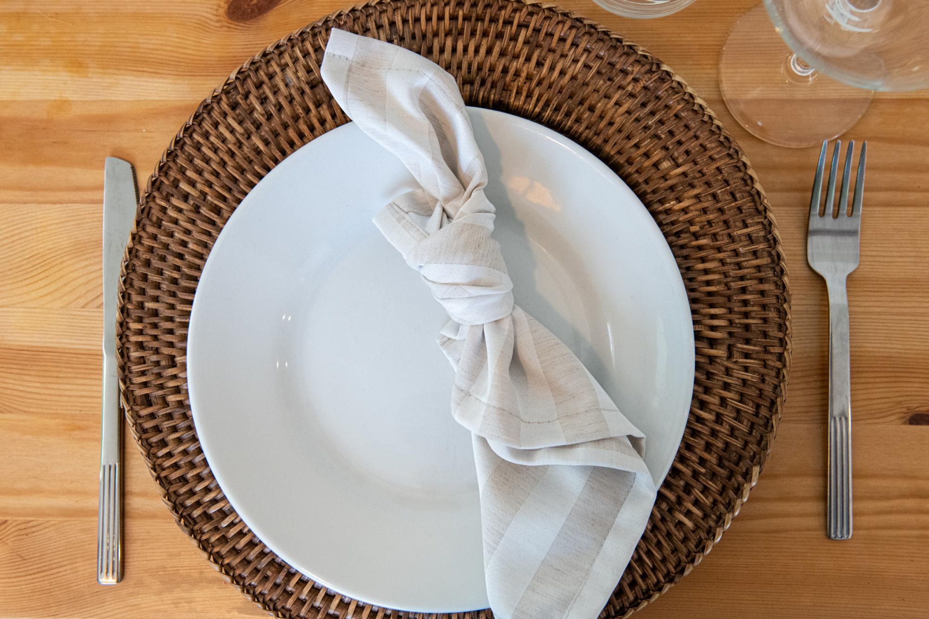 Une table à manger élégamment dressée, avec une assiette blanche, une serviette pliée et un verre d’eau.