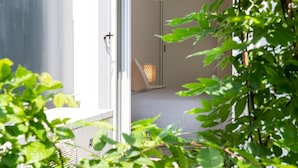 A modern room with a bed, a small table, and a chair. There is a window with blinds, and a plant is visible in the foreground. - La Casa di Guido in Gabicce Mare (Gabicce Mare)