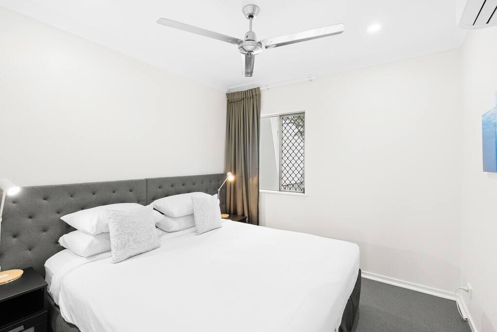 A neatly arranged bedroom with a bed, a nightstand, a ceiling fan, and a window with curtains.