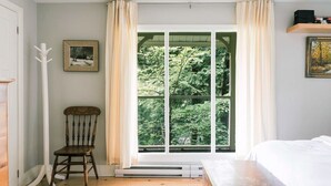 A bedroom with a large window, a wooden chair, and a bed.