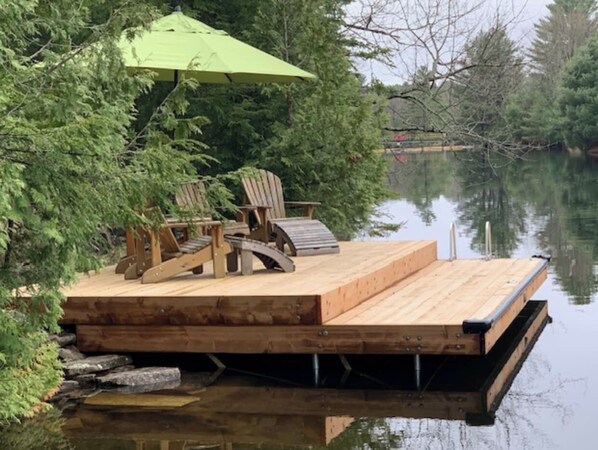 A wooden dock with a green umbrella, wooden chairs, and a small table.