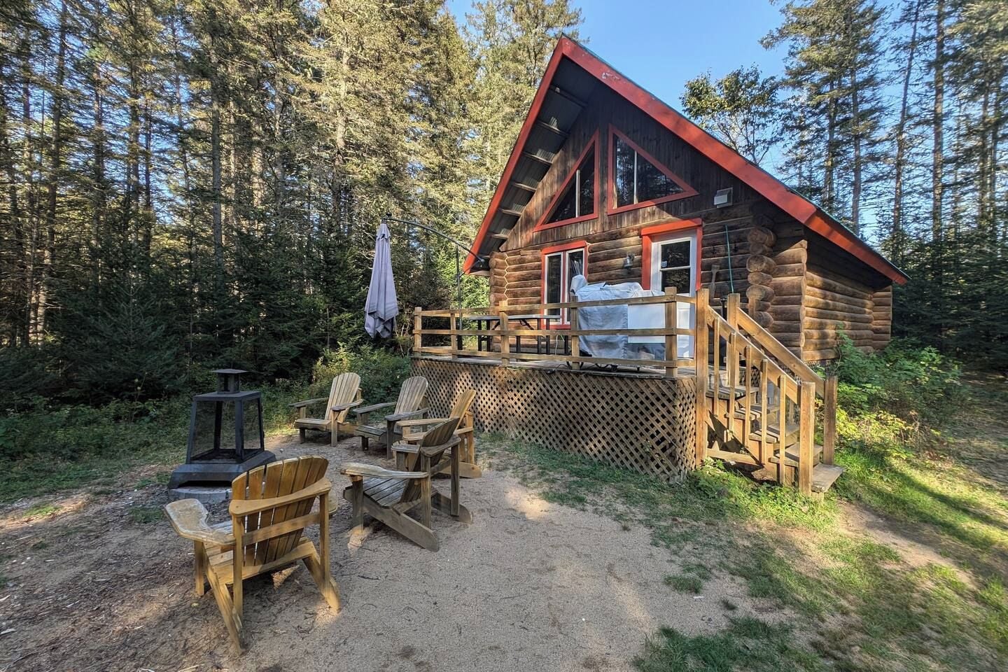 A log cabin with a deck, outdoor seating, and a forest backdrop.