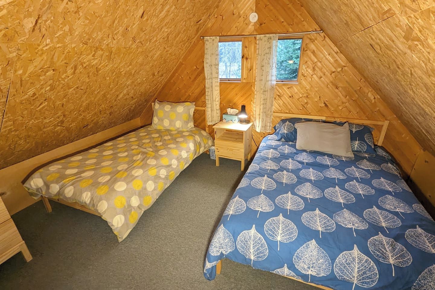 A small, cozy attic bedroom with two single beds, a nightstand, and a window with curtains.