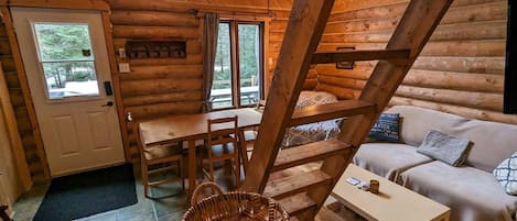 Interior de una cabaña de madera con comedor, sofá y escalera.