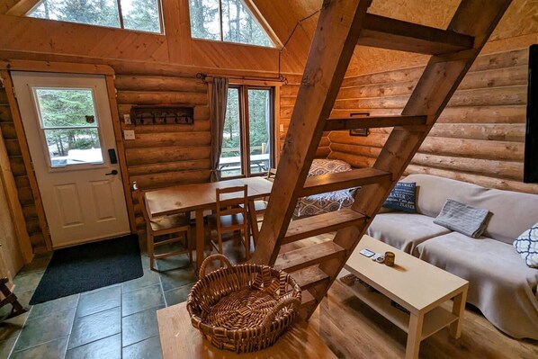A log cabin interior with a dining area, a sofa, and a staircase.