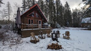 Een blokhut met een houten terras, buitenmeubels en een besneeerd landschap.