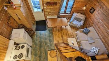 A compact cabin with a kitchenette, a dining area, and a seating area with a sofa and a patterned cushion.