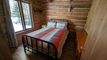 Une chambre à coucher située dans une cabane en rondins, avec un lit, une table de chevet, une fenêtre et un ventilateur de plafond.
