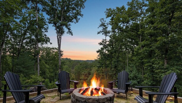 A stone fire pit with chairs around it, set in a forested area. - Valley Retreat! Sleeps 10 ~ Hot Tub ~ Fire Pit (Blue Ridge)