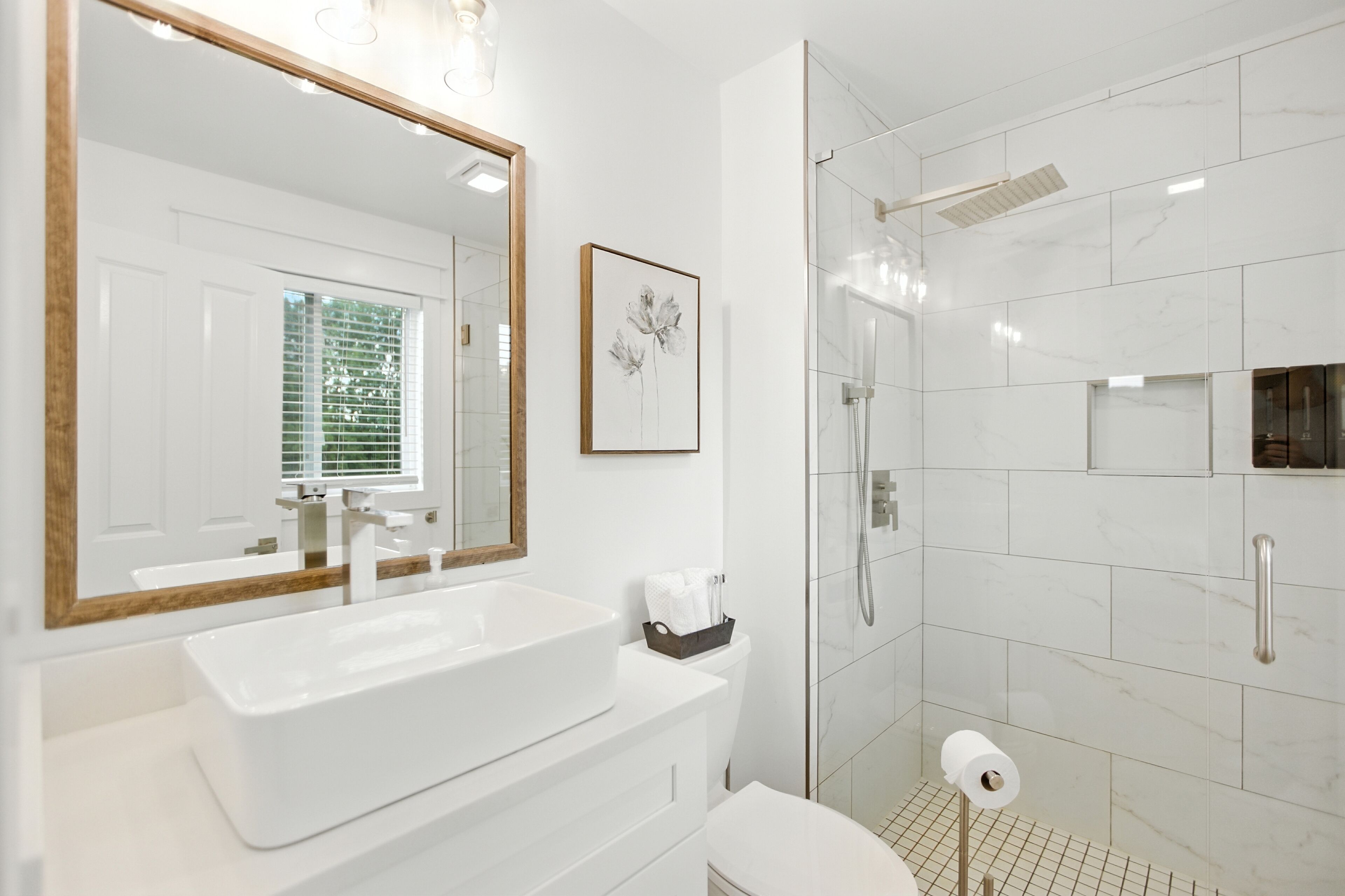 A modern bathroom with a large mirror, a white sink, a toilet, and a glass-enclosed shower.