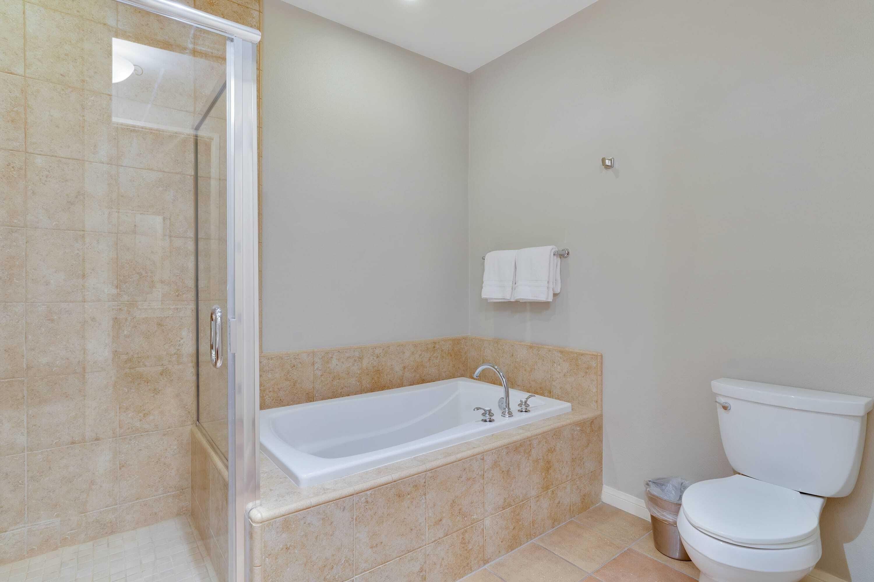 A bathroom with a glass-enclosed shower, a bathtub with a single faucet, and a toilet.