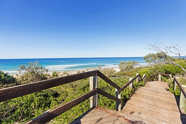 A wooden boardwalk leading to a beach with clear blue waters and a view of the ocean.